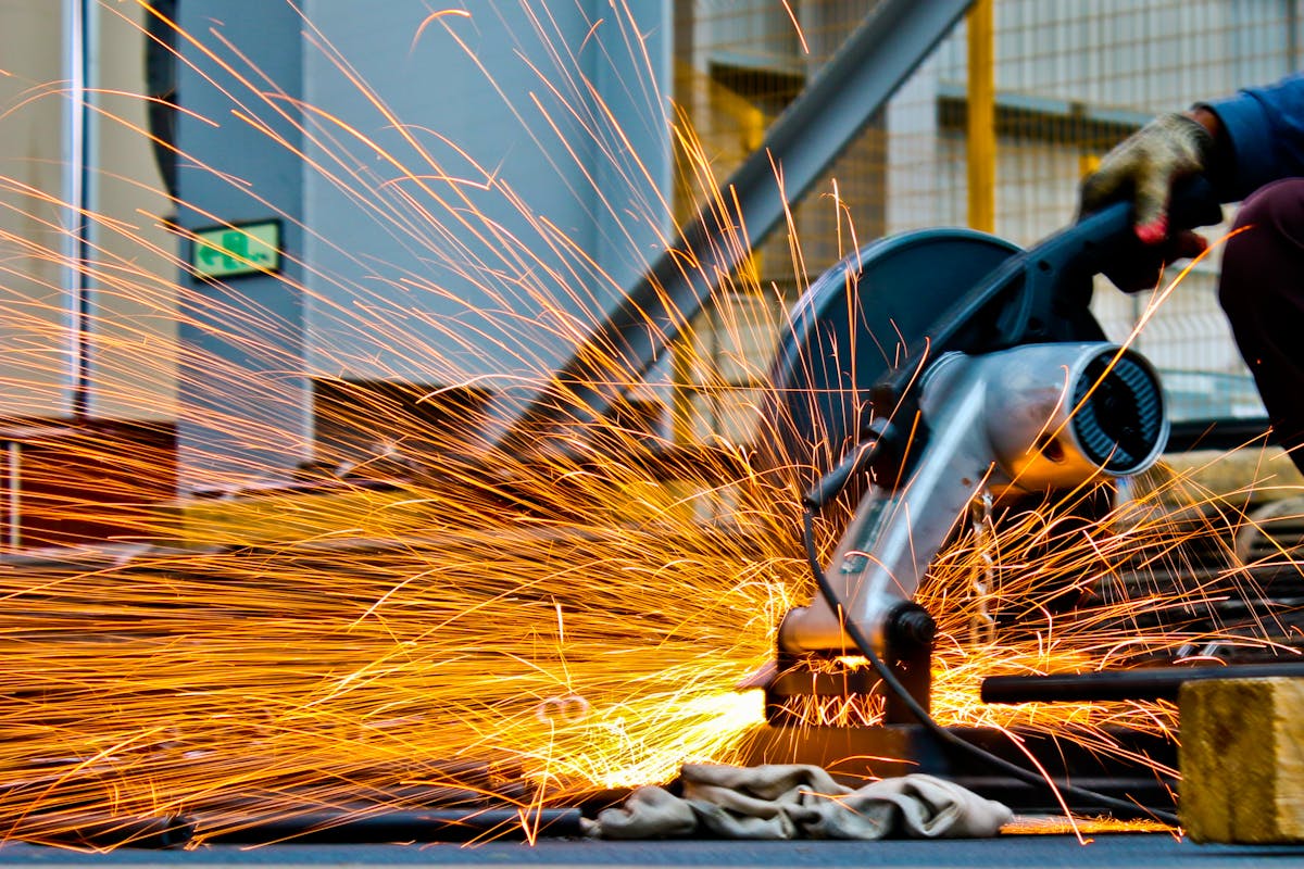 Worker operating angle grinder cutting metal with sparks