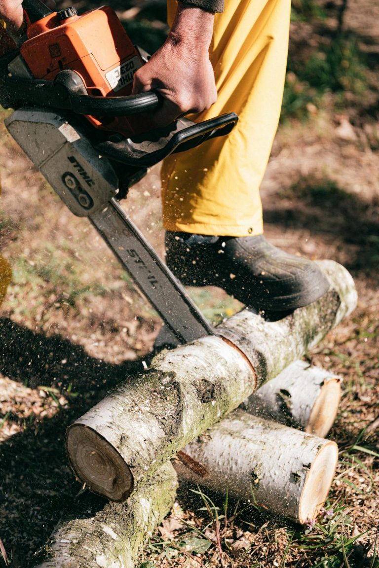 Person using chainsaw to cut wooden logs outdoors