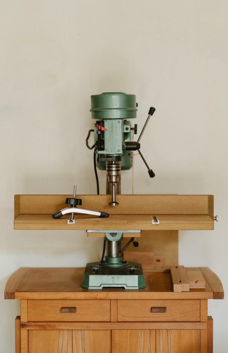 Green drill press on wooden workbench in workshop