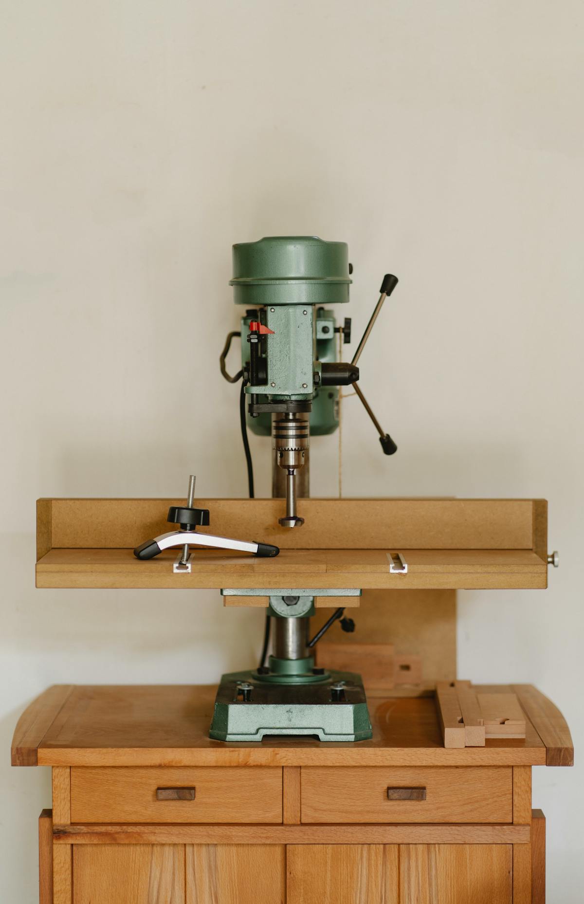 Green drill press on wooden workbench in workshop