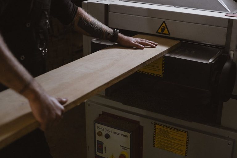 Carpenter using a benchtop thickness planer to smooth a wooden board in a workshop